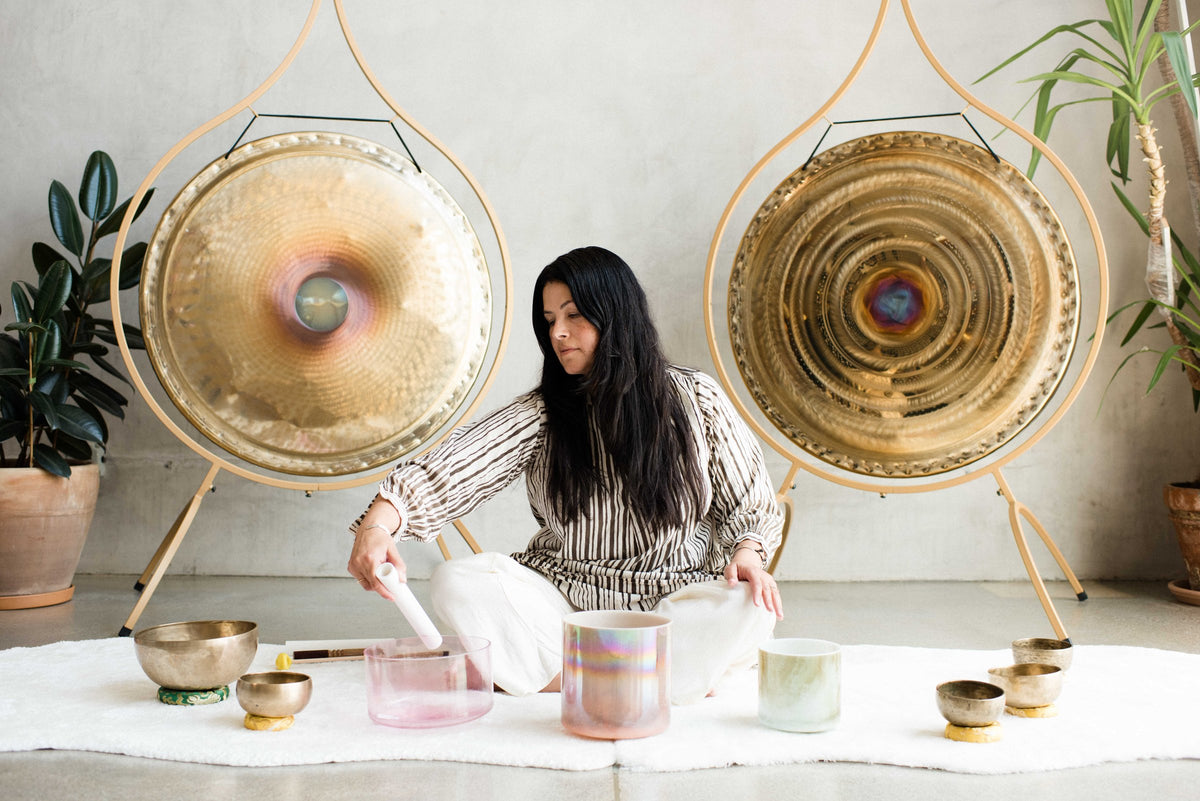 A practitioner playing crystal singing bowls between two gongs