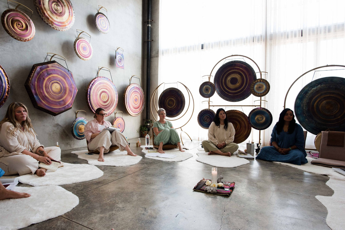 Students practicing with crystal singing bowls beneath the gong wall in the studio